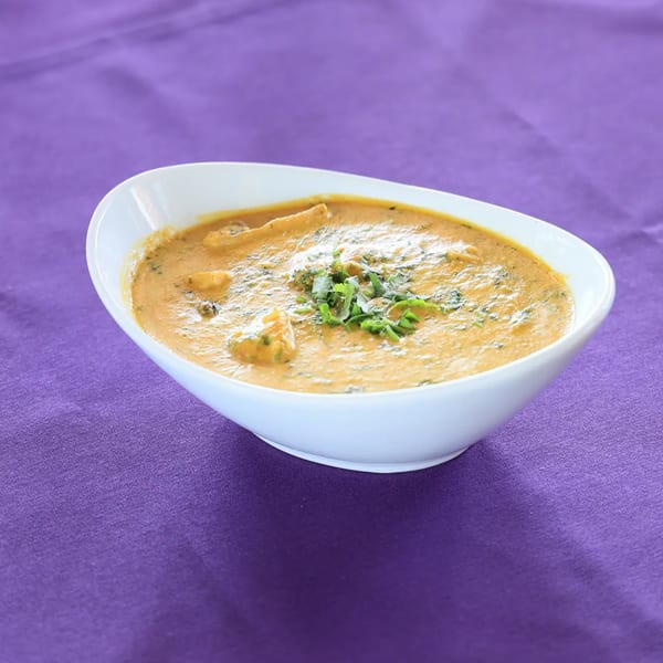 Zaika Indian Cuisine's creamy Indian curry, garnished with fresh herbs, in a white bowl on a purple tablecloth.