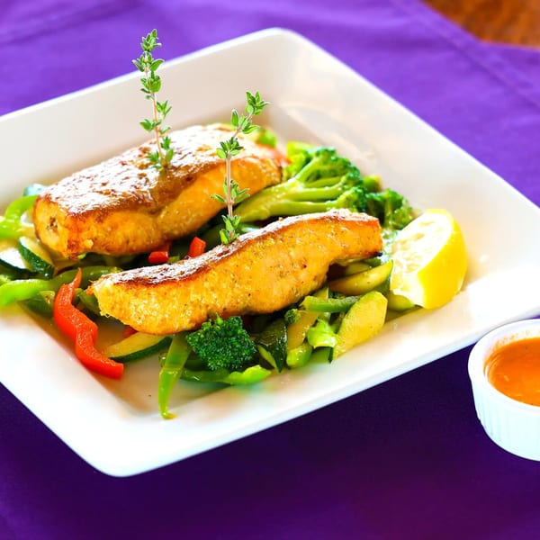 Two golden-brown fish fillets with thyme, mixed vegetables, a lemon wedge, and dipping sauce.