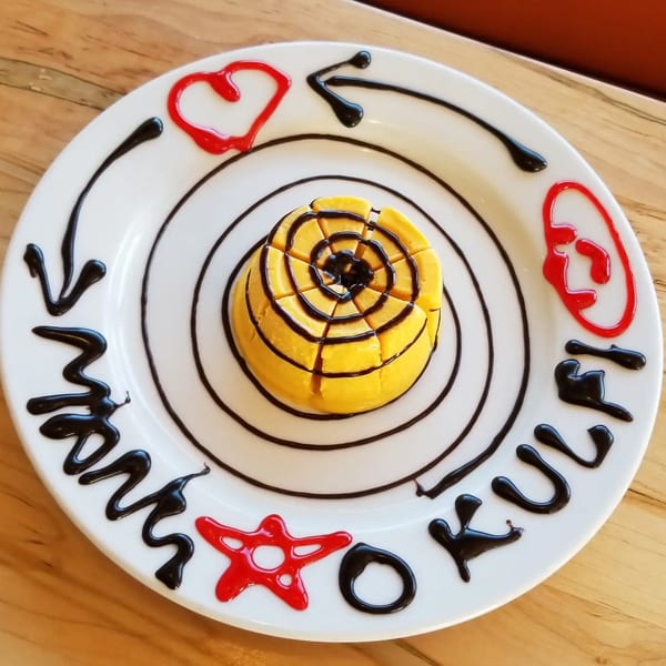 Mango Kulfi dessert with chocolate and red syrup decorations on a white plate.
